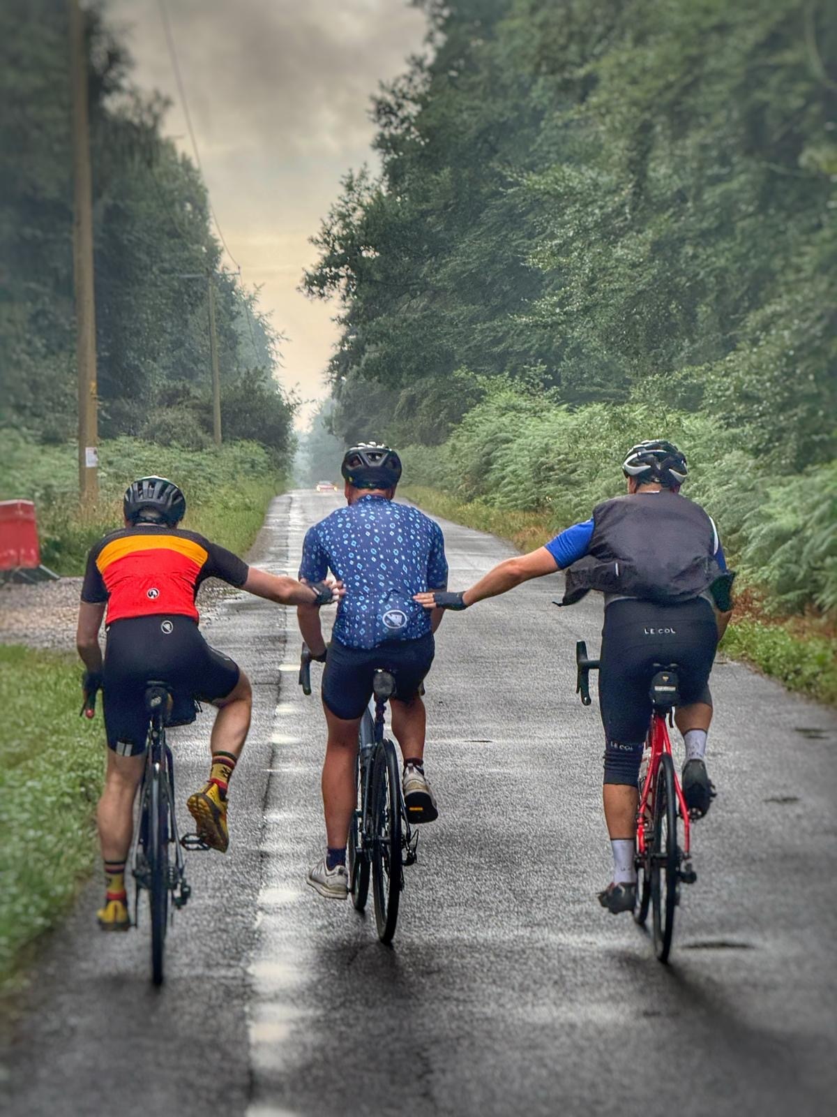 Three cyclists riding side by side on a wet forest road
